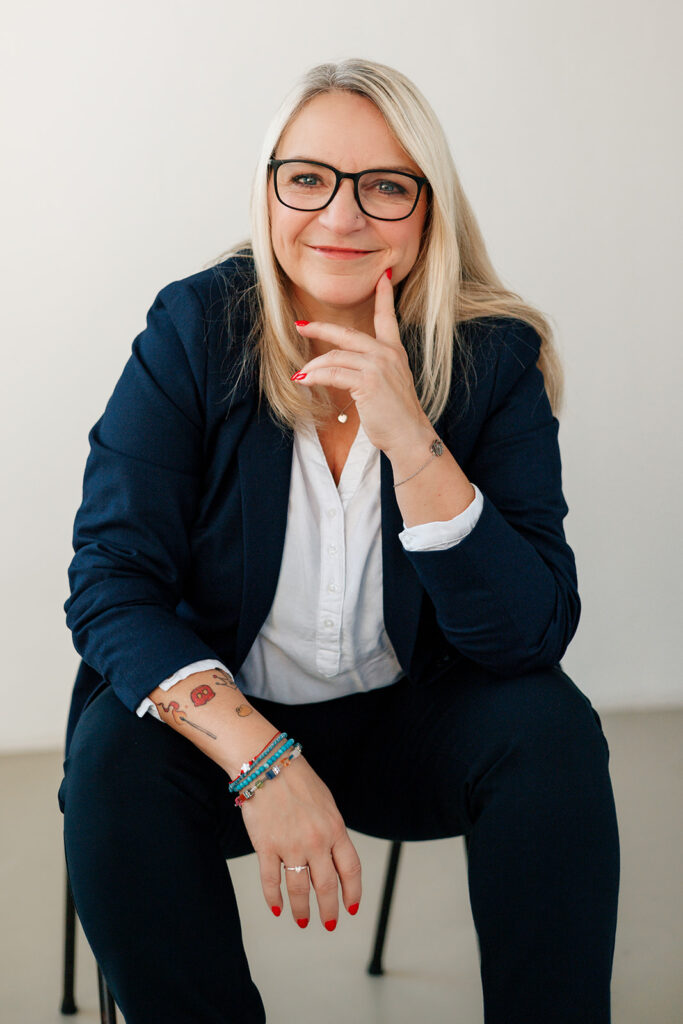 Petra Paulus sitzt im dunkelblauen Blazer und blickt nachdenklich in die Kamera.
